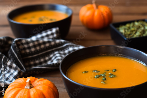 Two bowls of pumpkin soup on dark wood table