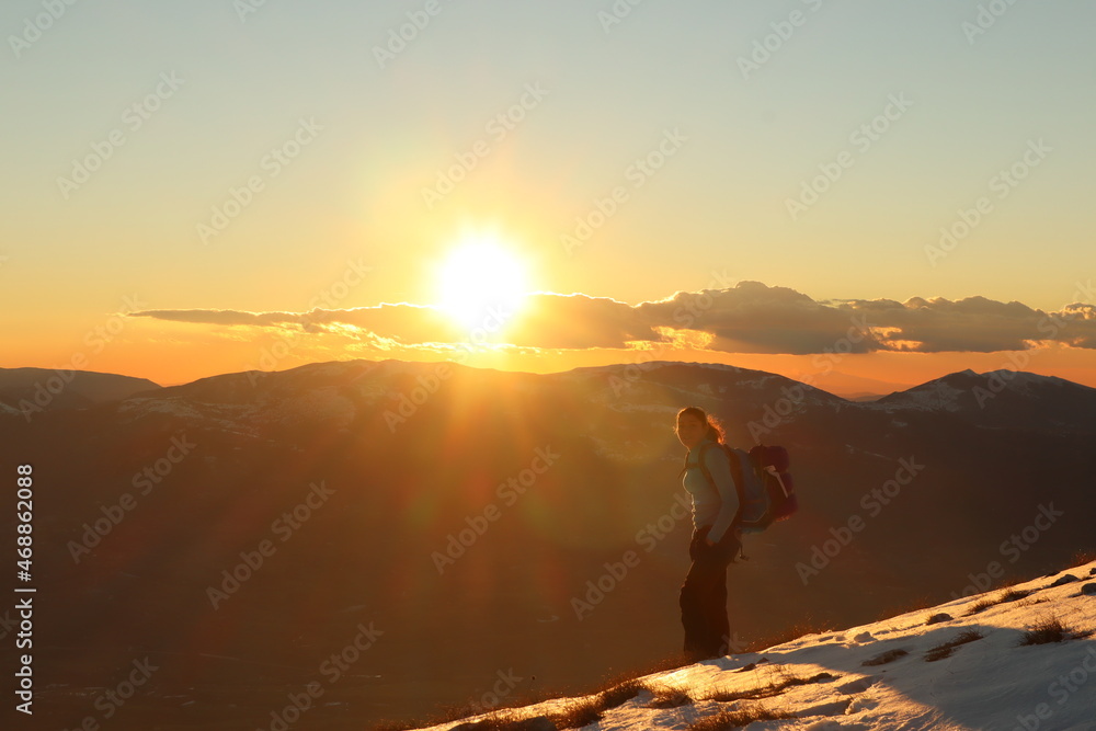 young caucasian female hiker on a mountain summit at sunset - golden hour in snowy landscape