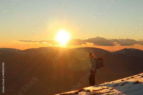 young caucasian female hiker on a mountain summit at sunset - golden hour in snowy landscape