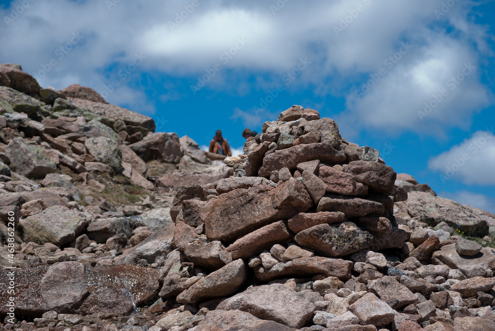 Pyramid of rocks to designate trail direction against blue sky background with clouds in the Rocky Mountains