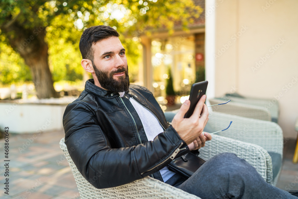 Side view portrait of one man adult modern caucasian male with beard sitting outdoor serious using mobile phone for video call at cafe in autumn day - leisure concept copy space Side view portrait of one man adult modern caucasian male with beard sitting outdoor serious using mobile phone for video call at cafe in autumn day - leisure concept copy space