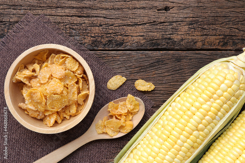 Cereal corn flakes in wooden bowl and corncobs on wooden table.