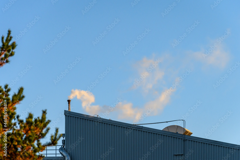 Industrial rooftop with pipe venting steam in early morning light against a blue sky
