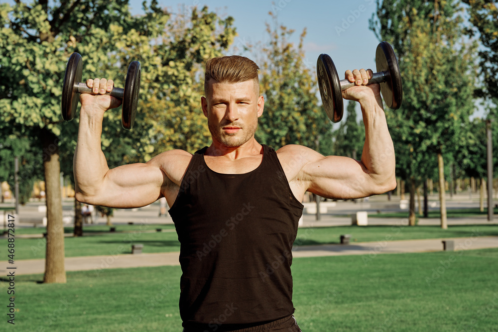 athletic man in black t-shirt with dumbbells in the park training athletic man in black t-shirt with dumbbells in the park training