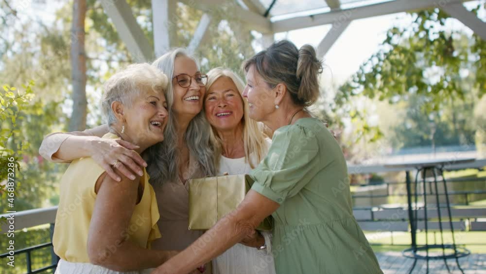 Happy senior woman getting presents from friends during celebration outdoors on patio Happy senior woman getting presents from friends during celebration outdoors on patio