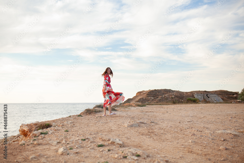 Beautiful woman in a long red dress near sea, a walk by the shore Beautiful woman in a long red dress near sea, a walk by the shore