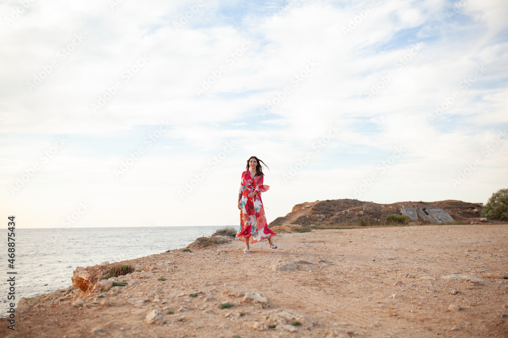 Beautiful woman in a long red dress near sea, a walk by the shore