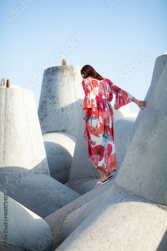 Beautiful woman in a long red dress near breakwater, a walk by the sea