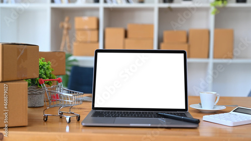 Mock up laptop computer, trolley and cardboard boxes on wooden table. Online shopping concept.