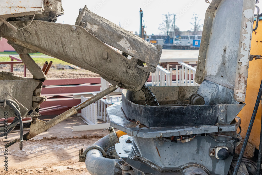 A concrete mixer truck pours concrete into a pump at a construction site.