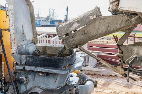 A concrete mixer truck pours concrete into a pump at a construction site.