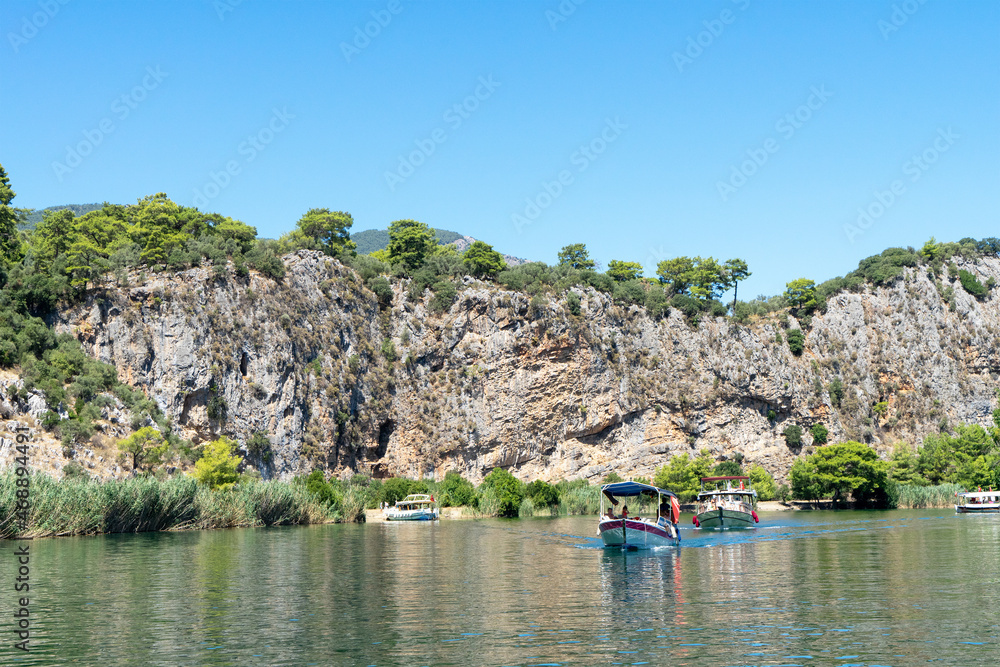 Tourist pleasure boats on the Dalyan River, next to the rocks, which contain the Lycian tombs, in Mugla Province located between the districts of Marmaris and Fethiye on the south-west coast of Turkey