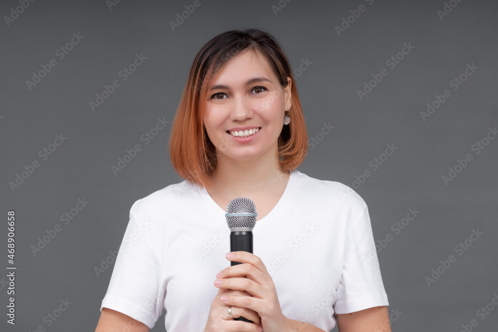 Young beautiful woman singing a song into a microphone while standing on a gray background Young beautiful woman singing a song into a microphone while standing on a gray background