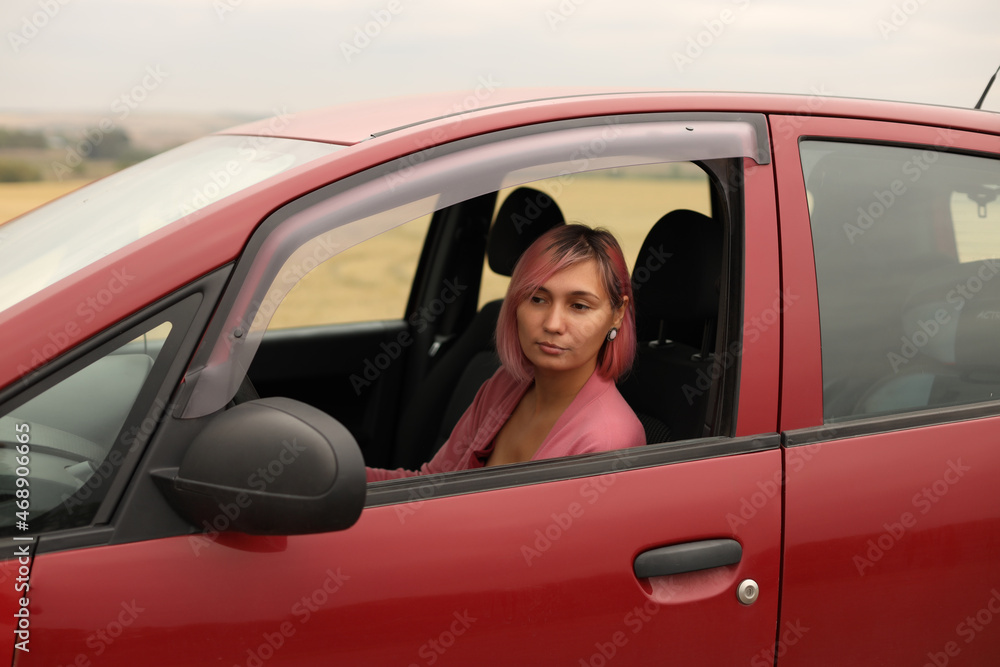A young woman with pink hair is driving her car