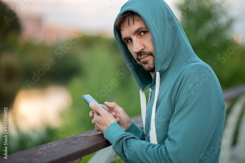 A young man in a hood with a phone in his hands. Hacker makes a hack through the telephone.