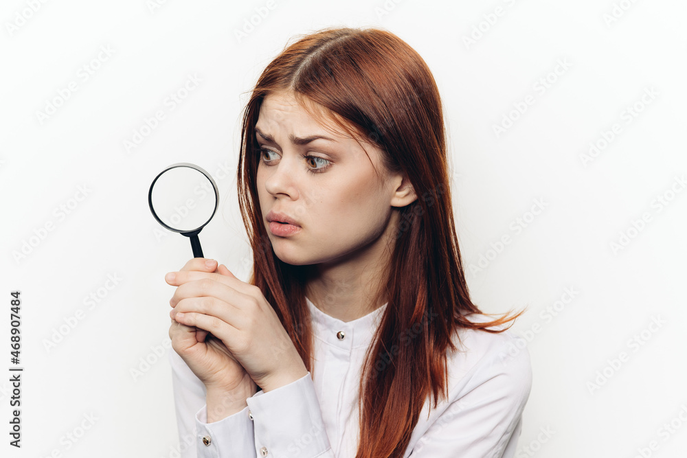 cheerful red-haired woman holding a magnifying glass near her face cheerful red-haired woman holding a magnifying glass near her face
