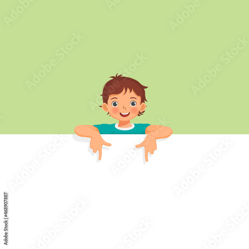 Little boy standing behind blank board peeking and pointing to empty banner with finger