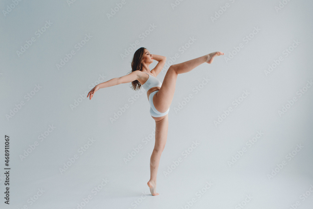 Fototapeta premium girl gymnast, in a white uniform, panties and top, in the studio on a white background shows exercises