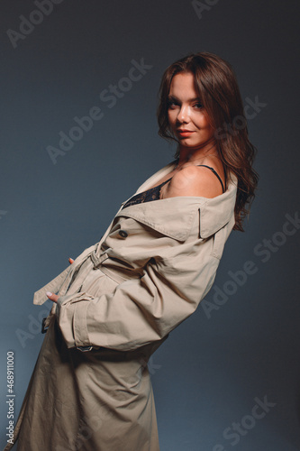 young beautiful girl in the studio, she sits on a chair on her wearing a trench coat and black lingerie, portrait
