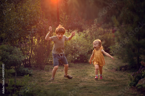 Cute baby girl and her funny older brother are running and fooling around during the beautiful sunset. Image with selective focus and toning