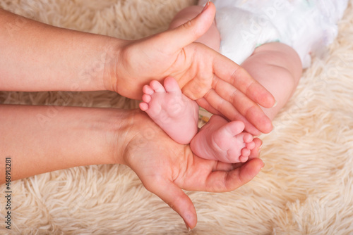 Mom holds in his hands a small baby foots. Small legs of a newborn baby in the hands of mother. Baby foot massage