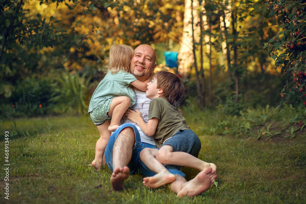 A boy and little girl are hugging their father in summer park. Image with selective focus and toning A boy and little girl are hugging their father in summer park. Image with selective focus and toning