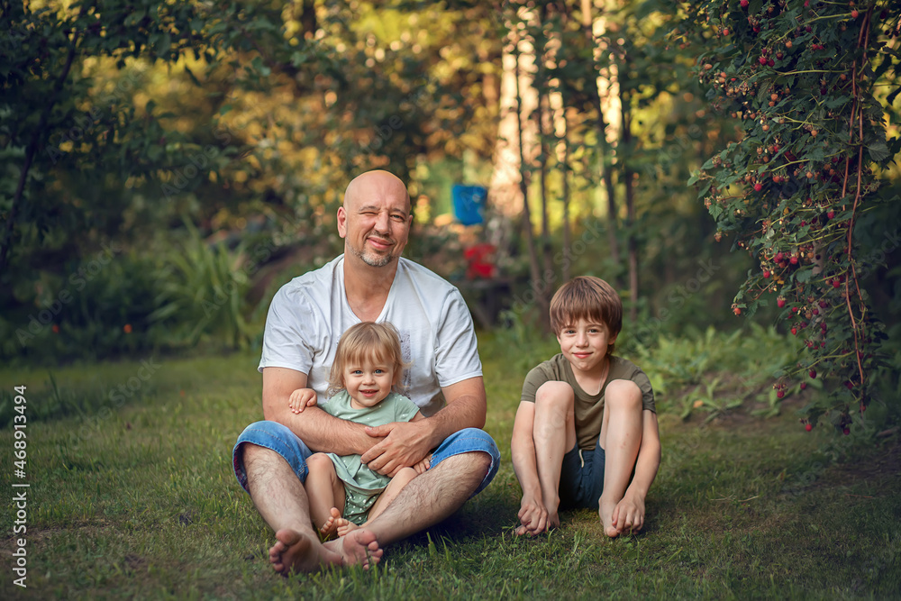 A boy and little girl are hugging their father in summer park. Image with selective focus and toning A boy and little girl are hugging their father in summer park. Image with selective focus and toning