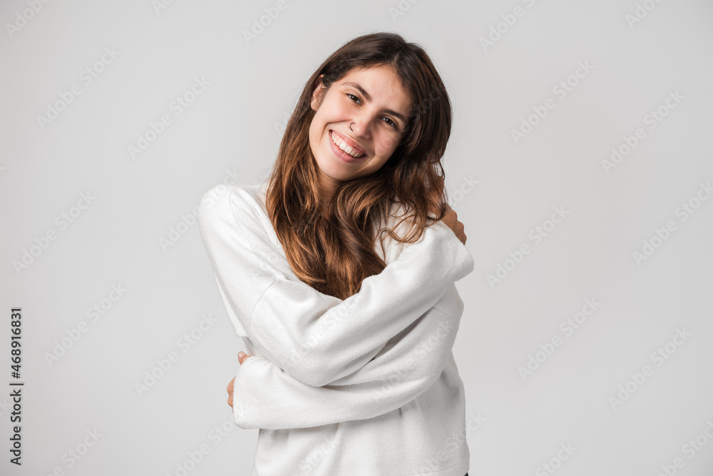 Portrait of beautiful young woman hugging herself tightly and smiling with pleasure, appreciating her appearance, self esteem concept. Indoor studio shot isolated on white background Portrait of beautiful young woman hugging herself tightly and smiling with pleasure, appreciating her appearance, self esteem concept. Indoor studio shot isolated on white background