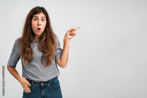 Funny woman pointing finger at copy space with surprised expression. People emotions concept. Indoor, studio shot on light white background