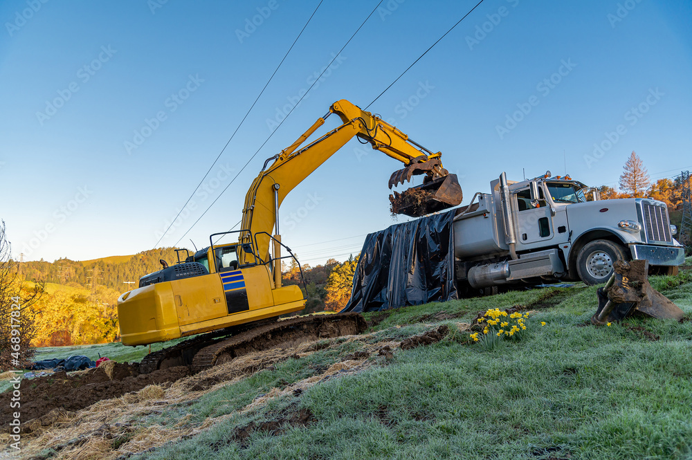 Yellow crawler excavator loads ground onto a large truck Yellow crawler excavator loads ground onto a large truck