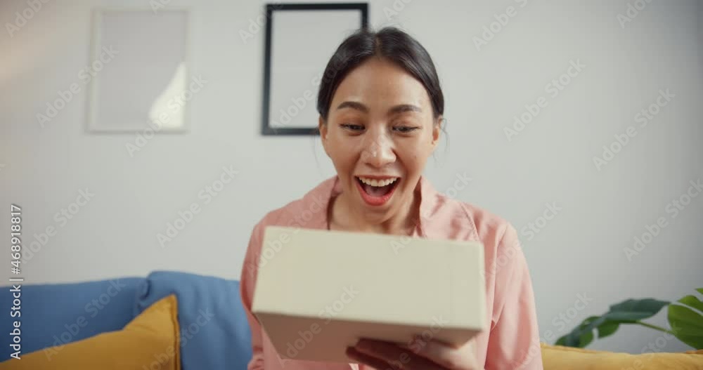 Happy beautiful Asia lady unboxing cardboard delivery package from online marketplace in living room at house. Satisfied shopper in internet unboxing goods, Online shopping and delivery concept. Happy beautiful Asia lady unboxing cardboard delivery package from online marketplace in living room at house. Satisfied shopper in internet unboxing goods, Online shopping and delivery concept.