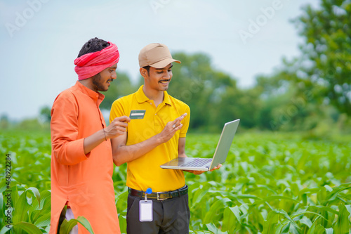 Young indian banker or agronomist showing some detail to farmers in laptop at agriculture field.