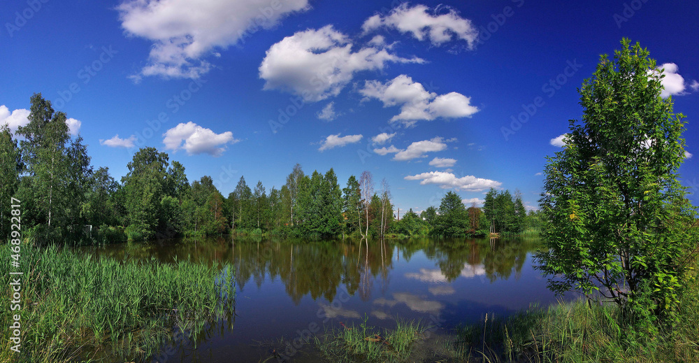 A lake in the forest with bright blue sky and clouds reflecting in water