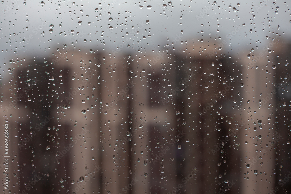 Macro raindrops on window with cityscape in the afternoon with grey sky. Blurred urban skyline background with water drops. Rainy season concept. Macro raindrops on window with cityscape in the afternoon with grey sky. Blurred urban skyline background with water drops. Rainy season concept.