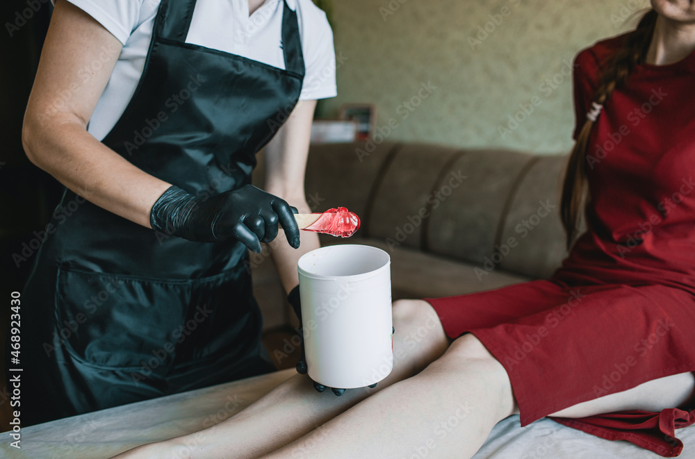 Carrying out the depilation procedure . A confident professional depilation master is preparing to apply wax to the client's feet Carrying out the depilation procedure . A confident professional depilation master is preparing to apply wax to the client's feet