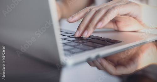 Woman hands typing on laptop computer keyboard on glass table, close up