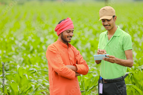 Young indian agronomist showing some information to farmer in smartphone at agriculture field.