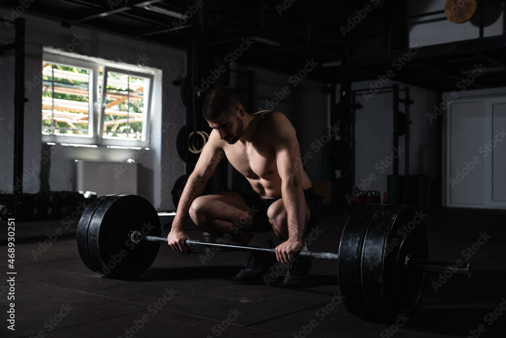 Young strong sweaty active bodybuilder and weightlifter muscular man with big muscles taking a break in the gym from the hardcore workout cross training and taking a breath after doing heavy deadlifts Young strong sweaty active bodybuilder and weightlifter muscular man with big muscles taking a break in the gym from the hardcore workout cross training and taking a breath after doing heavy deadlifts