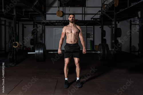 Young sweaty strong muscular fit man with big muscles holding heavy barbell weight and starting hardcore weightlifting or deadlift workout cross training in the gym real people exercising