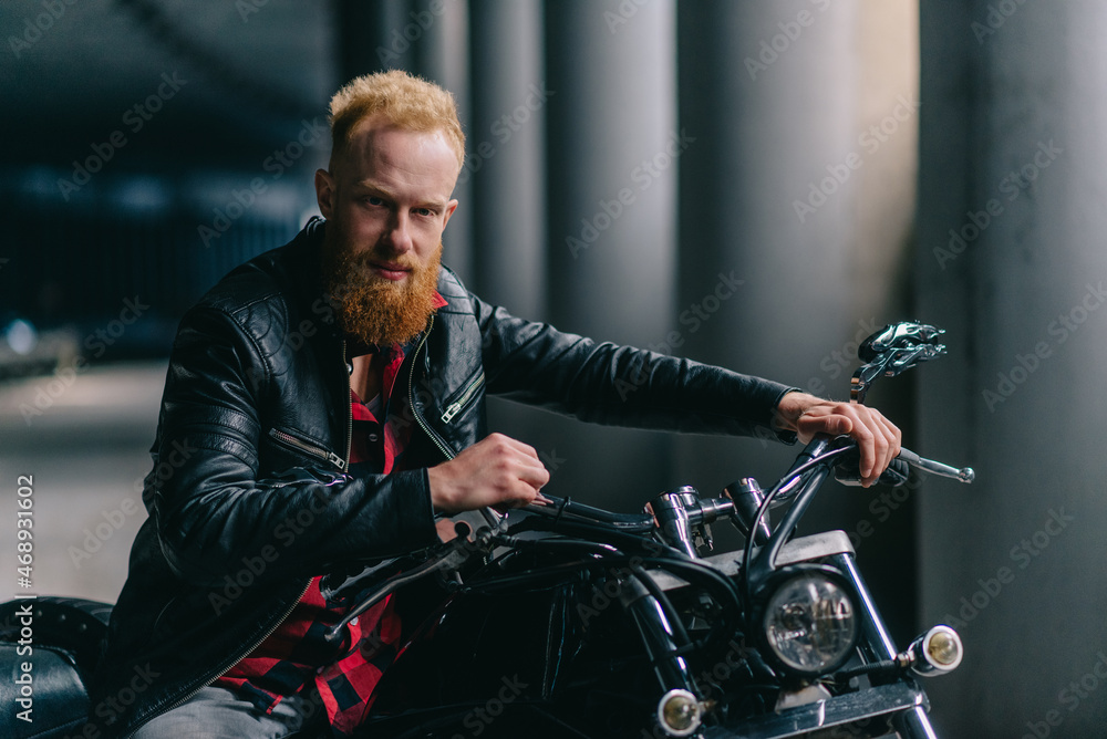 Portrait of young biker. Bearded red-haired man sits astride motorbike and looks at camera. Portrait of young biker. Bearded red-haired man sits astride motorbike and looks at camera.
