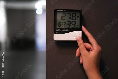 woman adjusts the psychrometer at home. device for measuring humidity and temperature on a dark wall close-up	 photo