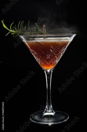 Alcoholic cocktail Cosmopolitan cocktail decorated with rosemary on martini glass and spray  on black background. Copy Space.