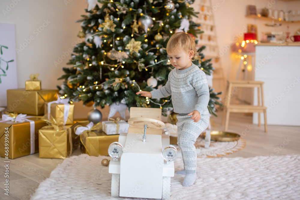 Adorable baby girl sitting near Christmas tree with festive lights and xmas gifts. Chrismas and New Year. Adorable baby girl sitting near Christmas tree with festive lights and xmas gifts. Chrismas and New Year.