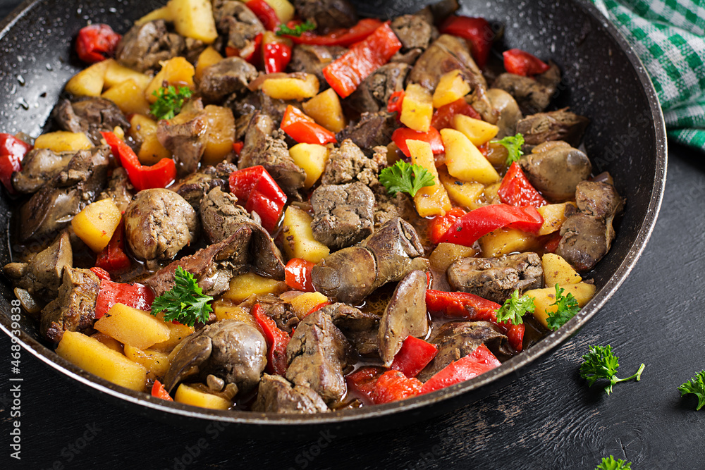 Fried chicken liver with apples and sweet peppers in iron skillet.