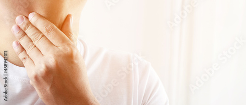sore throat pain. Closeup of young man sick holding her inflamed throat using hands to touch the ill neck in blue shirt on gray background. Medical and healthcare concept. Focus red on to show pain.