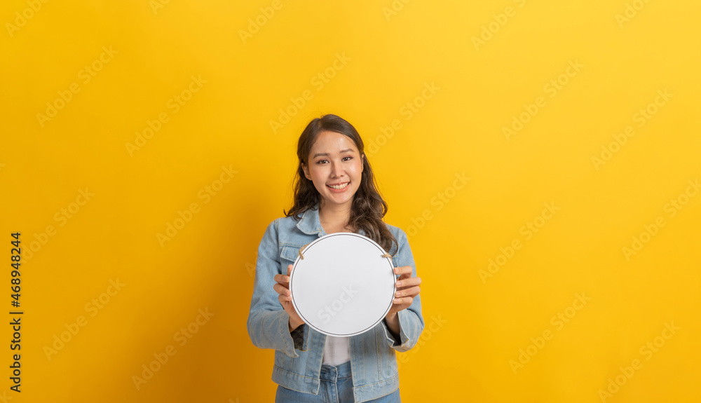Advertisement. happy young asian pretty woman in denim Jacket clothing smiling and hold blank sign board with copy space area for text on yellow background, online marketing, announcement concept Advertisement. happy young asian pretty woman in denim Jacket clothing smiling and hold blank sign board with copy space area for text on yellow background, online marketing, announcement concept