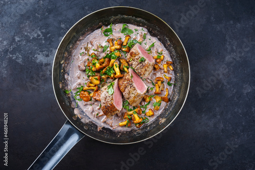 Fried dry aged pork fillet chateaubriand medallion steak natural with chanterelles in walnut cream sauce served as top view in a classic skillet on black background