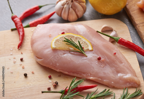 raw chicken fillet with garlic, pepper and rosemary on wooden on chopping board. fresh fillet. fresh chicken meat, chicken fillet with spices at black stone table. top view with copy space..