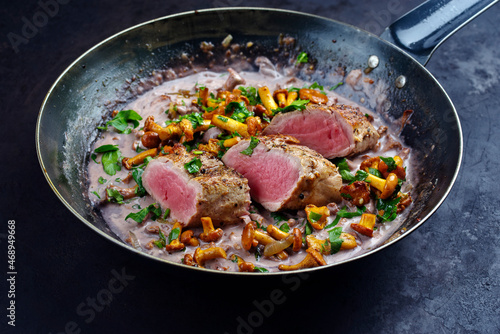 Gebratenes dry aged Schweinefilet Chateaubriand Medaillon Steak natur mit Pfifferlingen in Walnuss Creme Sauce serviert als Draufsicht in einer klassischen Bratpfanne auf schwarzen Hintergrund