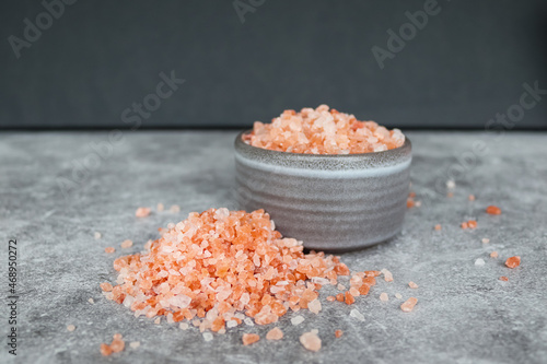 Heap of pink Himalayan rock coarse salt on the table next to a gray bowl with salt